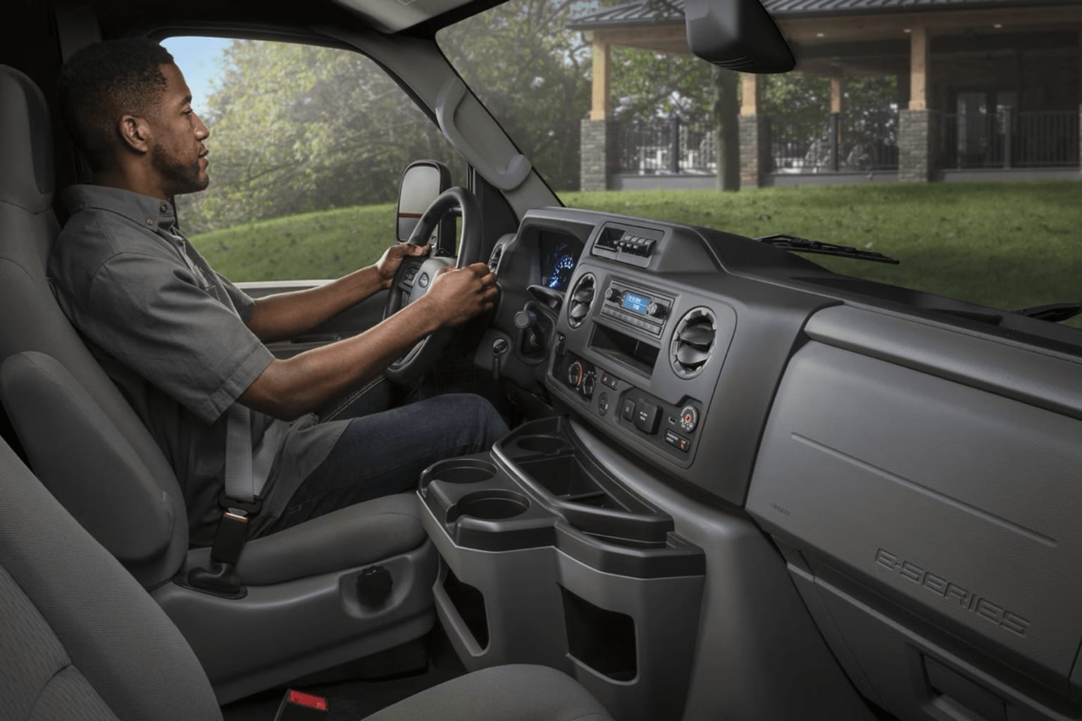 Interior of a vehicle with a person driving, surrounded by a park setting with trees and greenery visible through the windshield.