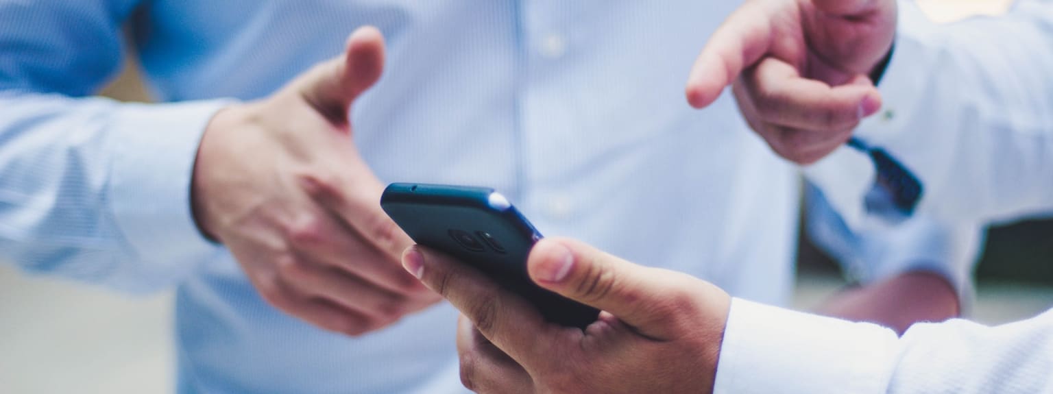 a man in a blue shirt is holding a smart phone in his hands and pointing at it with both hands