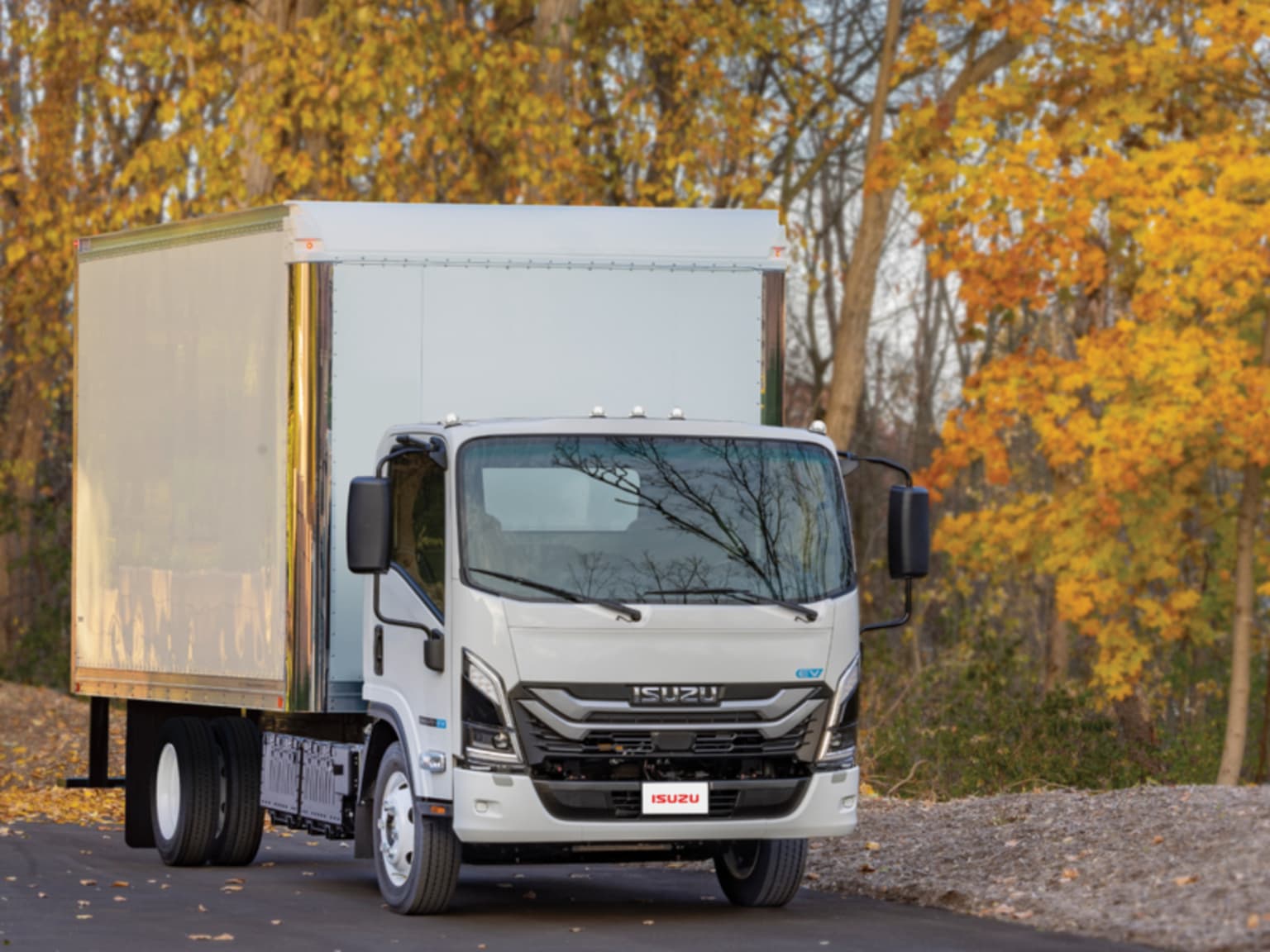 A white box truck parked on a road with autumn trees in the background.