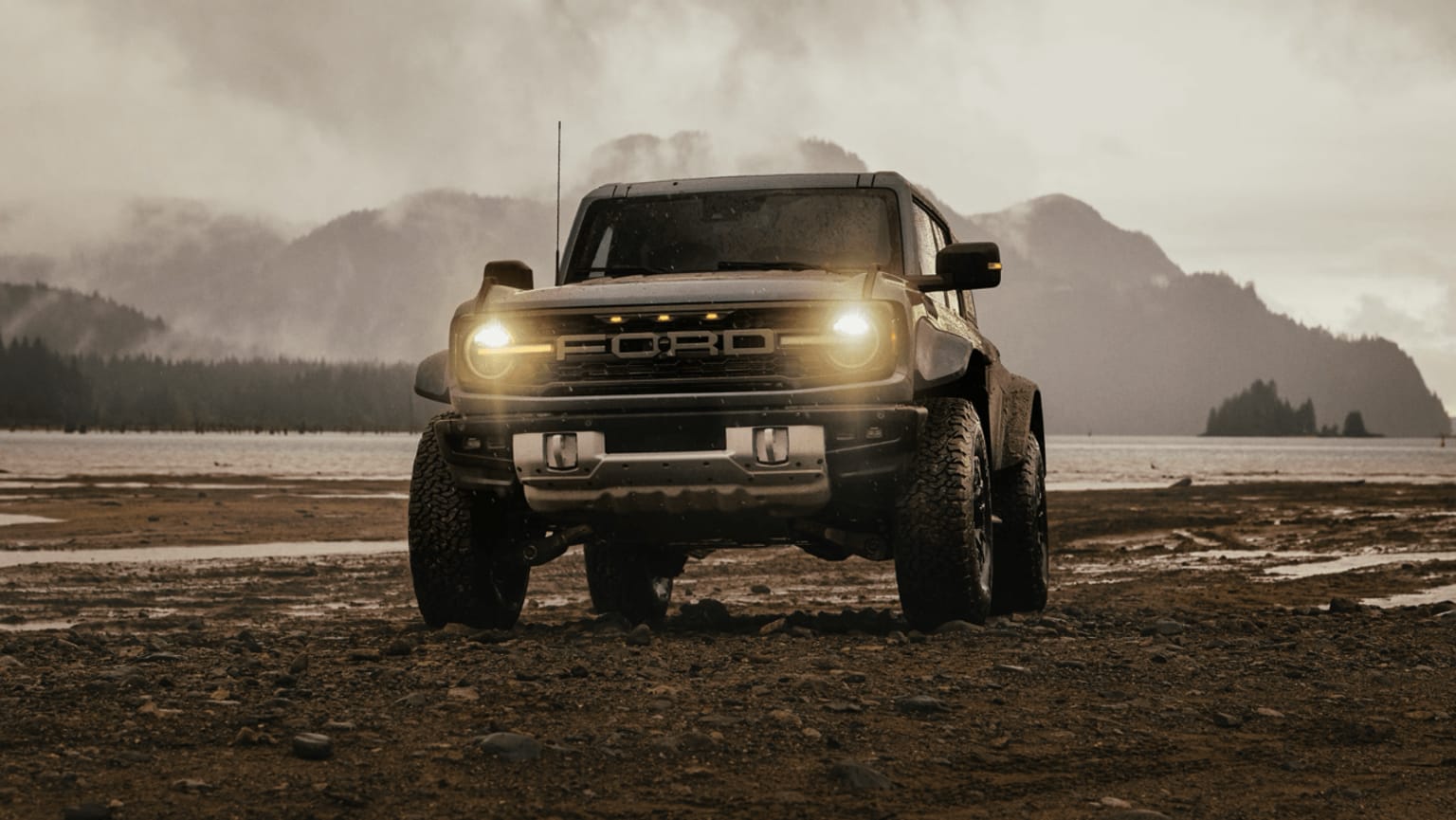 An off-road vehicle with powerful headlights illuminating a misty, mountainous landscape in the background.
