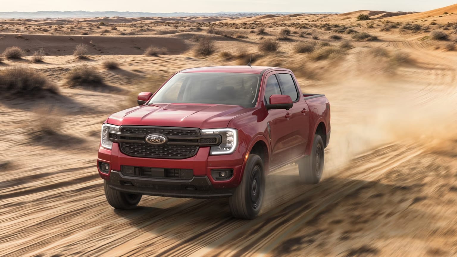 A red pickup truck speeding through a desert landscape with rolling hills and mountains in the background.