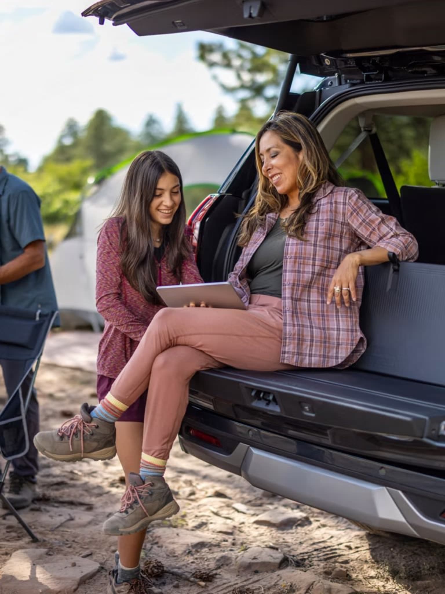 Two young women sitting in the back of an SUV, surrounded by a natural outdoor setting with trees and rocks in the background.