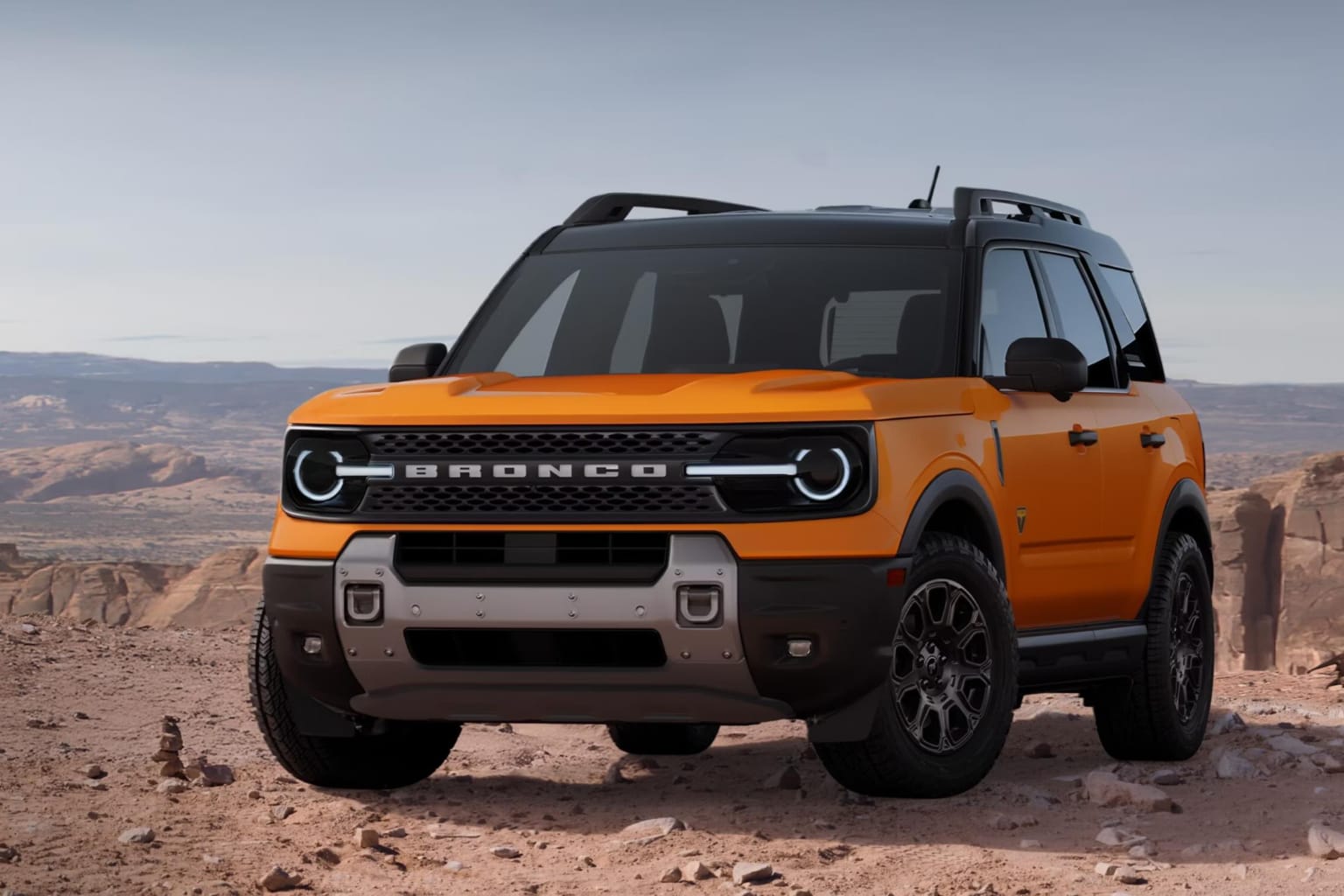 An orange SUV sits on a rocky desert terrain against a backdrop of distant red rock formations and a clear sky.