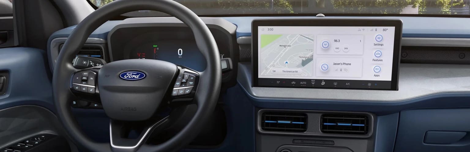 Interior of a vehicle, featuring a steering wheel and dashboard display with navigation system and controls.
