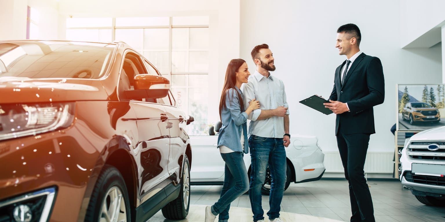 A couple examining a vehicle in a car showroom with a salesperson holding a clipboard.