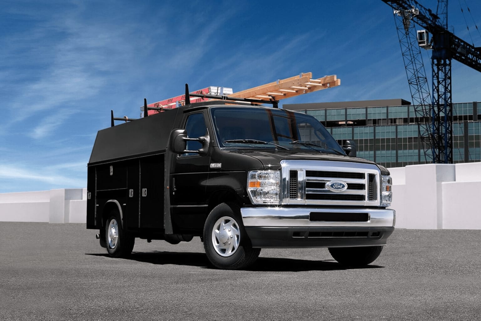 A black utility truck with a ladder rack on the roof is in the foreground, against a backdrop of a construction site with a crane visible in the distance.