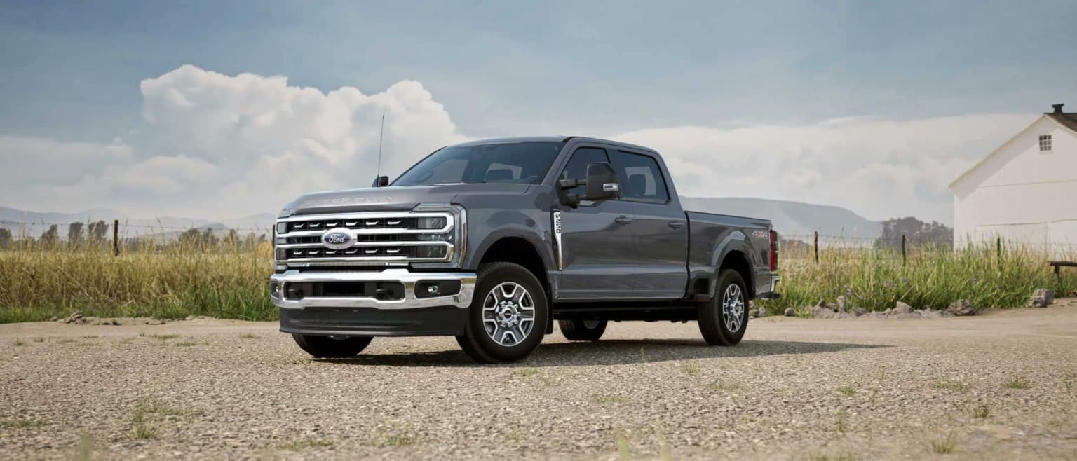 A rugged pickup truck in gray color in a grassy field with cloudy skies in the background.