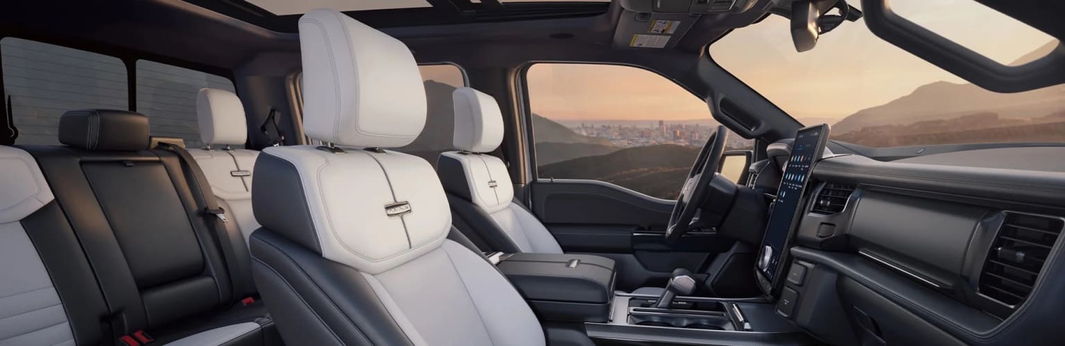 The image shows the interior of a vehicle, with white leather seats and a dashboard visible. In the background, a cityscape can be seen through the windshield, suggesting the vehicle is parked or driving with a view of the city.