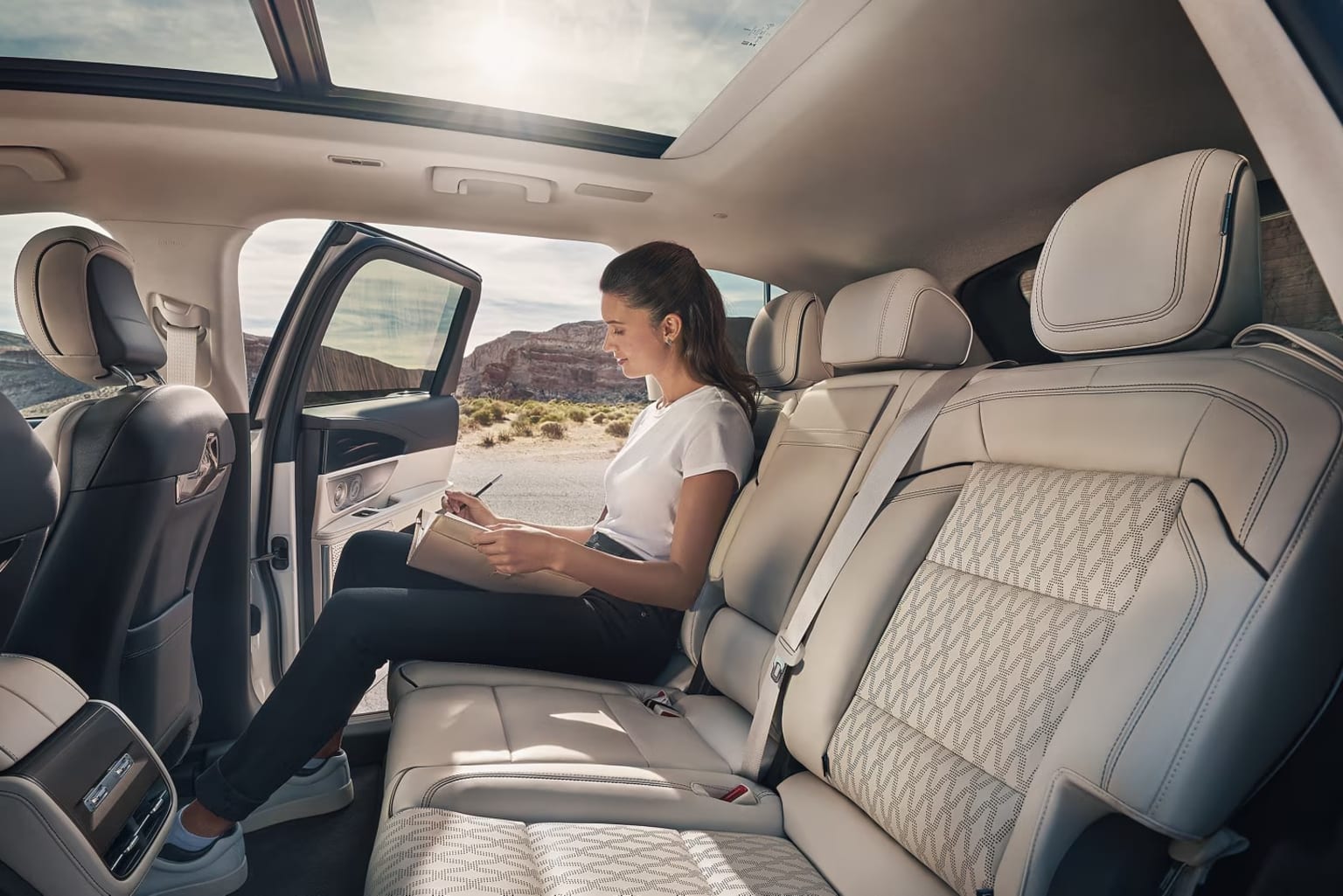 A person is seated in the back of a vehicle, surrounded by the interior of the car and a scenic desert landscape visible through the windows.