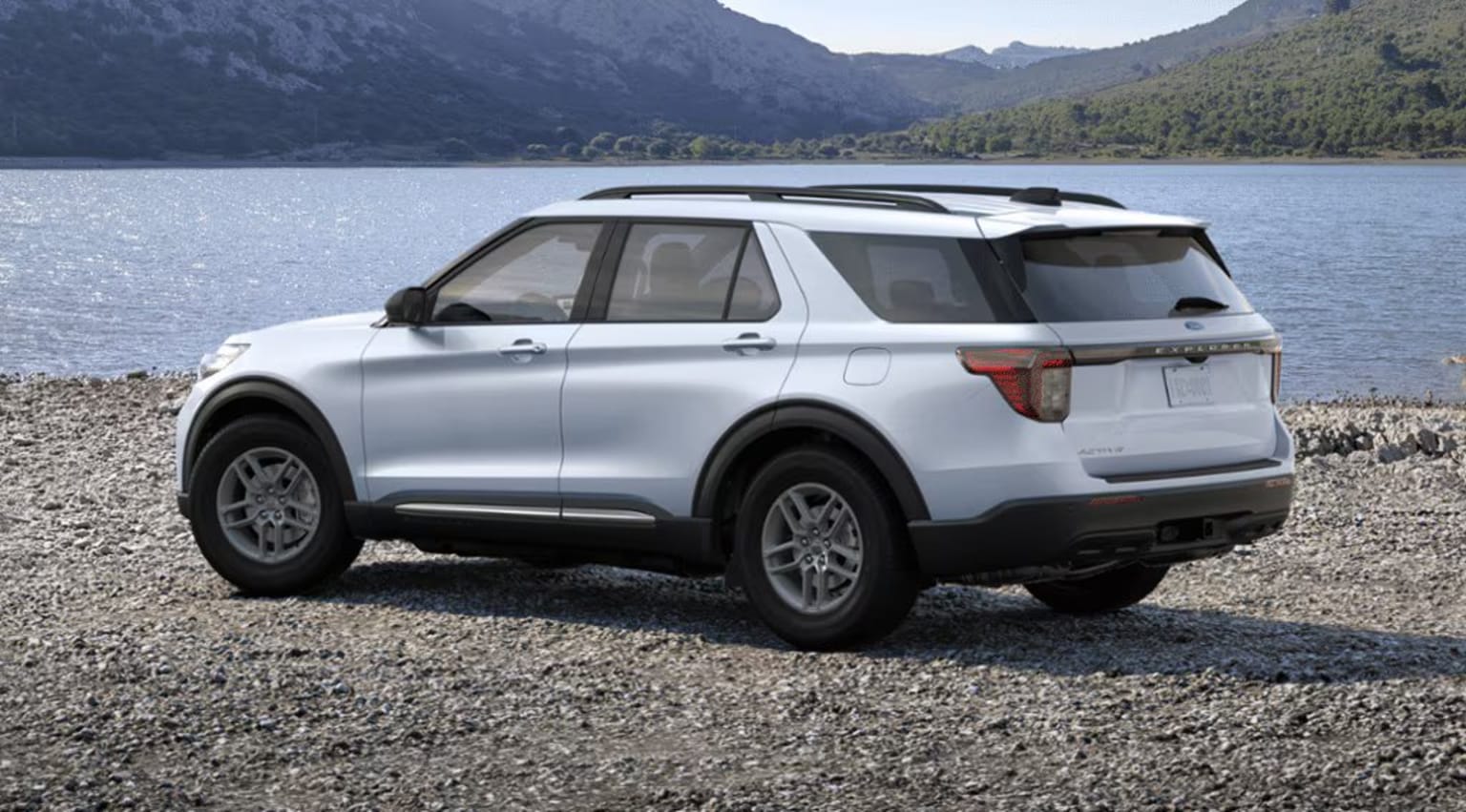 2025 Ford Explorer Exterior Color Option Space White Metallic parked on a rocky shore, with a scenic lake and mountains in the background.