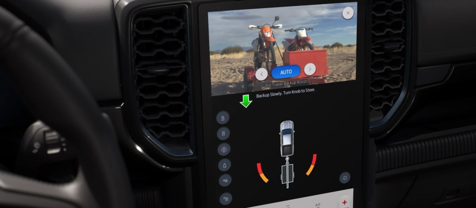 The image shows a motorcycle in the foreground, with a display screen in the center that appears to be showing a video or image of two motorcycles in a rural, grassy landscape.