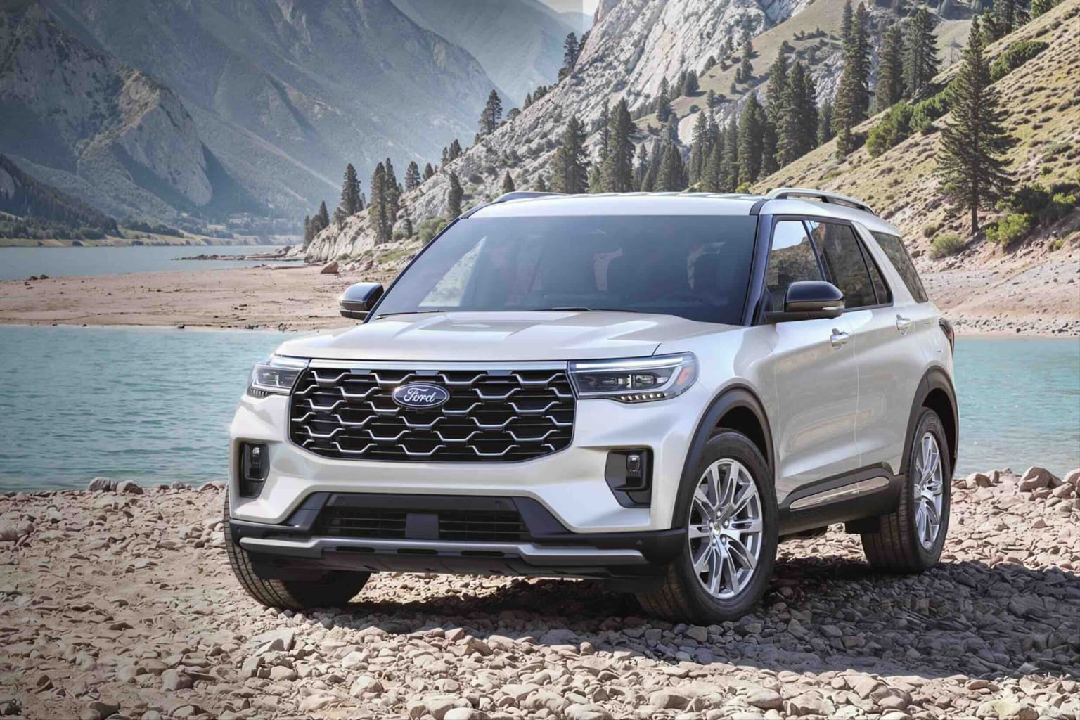 A white SUV is parked on a rocky shore with a lake and mountains in the background.