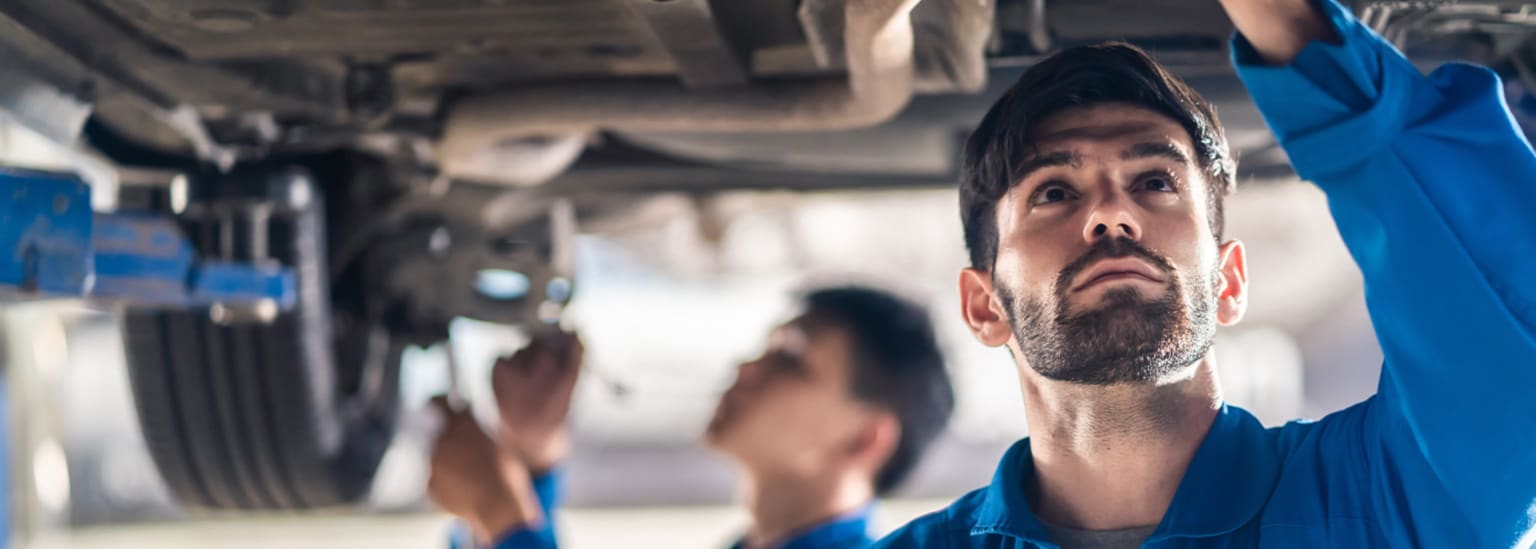 Mechanics working underneath a car, one looking up intently.