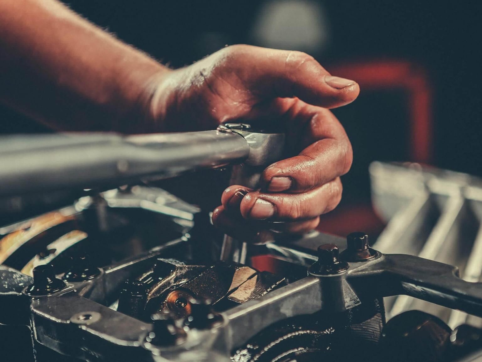 Hands of a mechanic working on a mechanical device, with various tools and parts visible in the background.