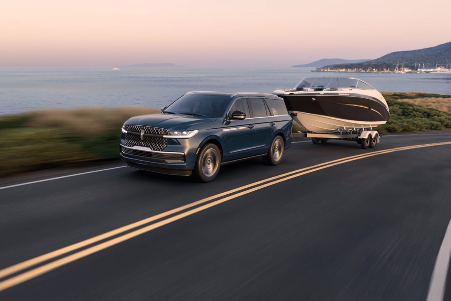An SUV towing a boat trailer on a coastal road with a sunset and ocean view in the background.