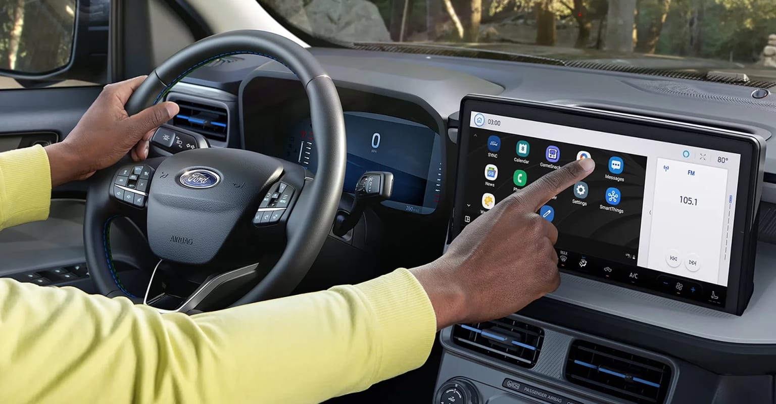 The image shows the interior of a vehicle, with a person's hands on the steering wheel and a touchscreen display in the center console.