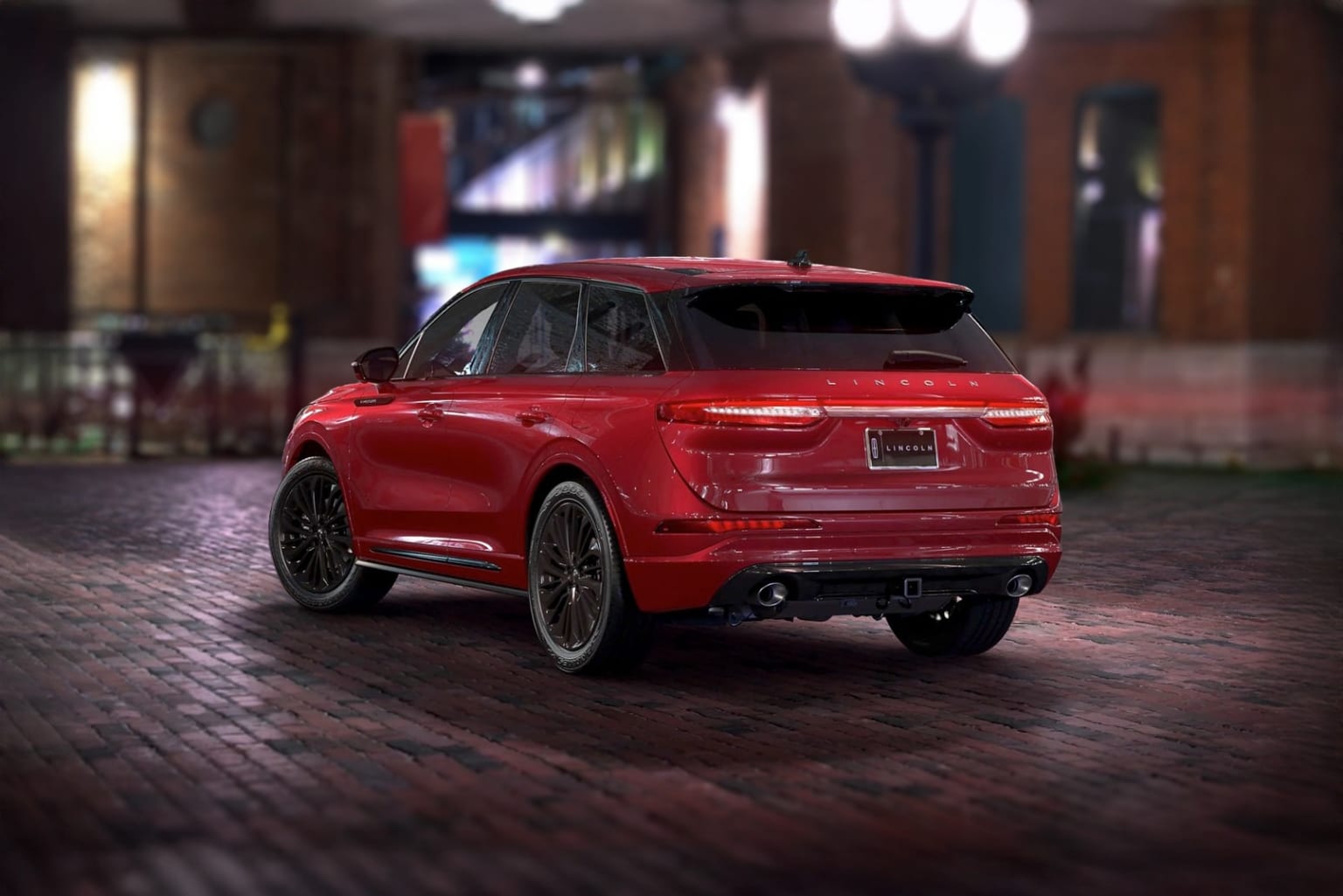 A sleek, red SUV parked on a cobblestone street with a dimly lit background of buildings and structures.