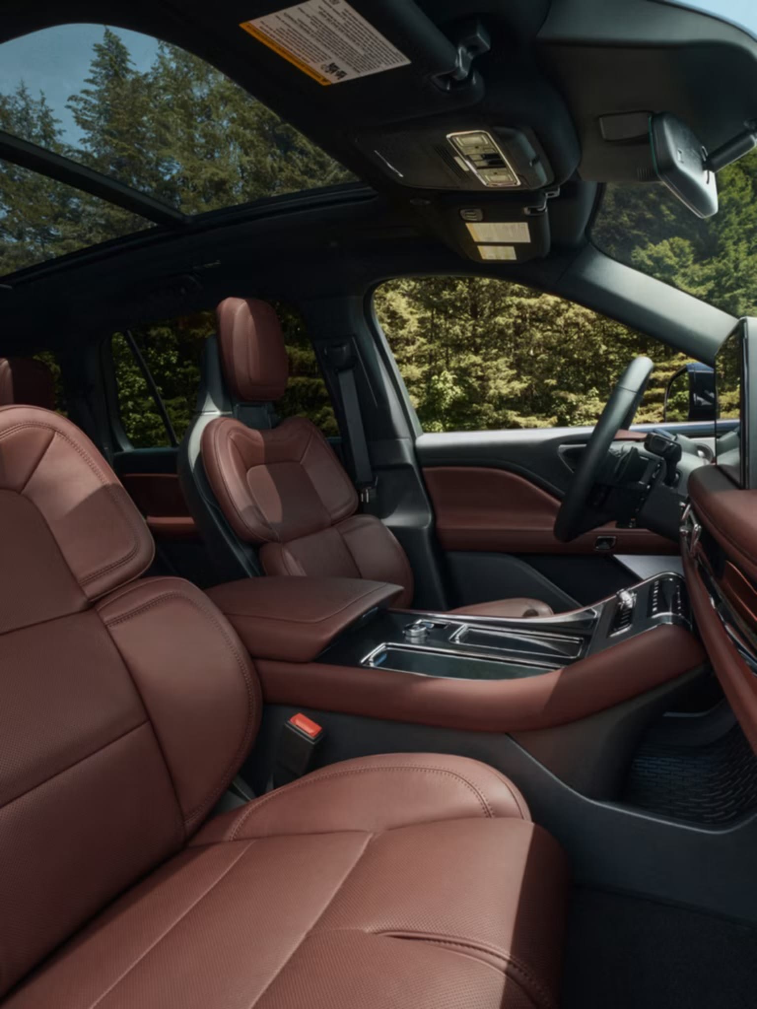 Interior of a luxury vehicle with plush leather seats and a modern dashboard, set against a background of a forested area with trees and greenery visible through the windows.