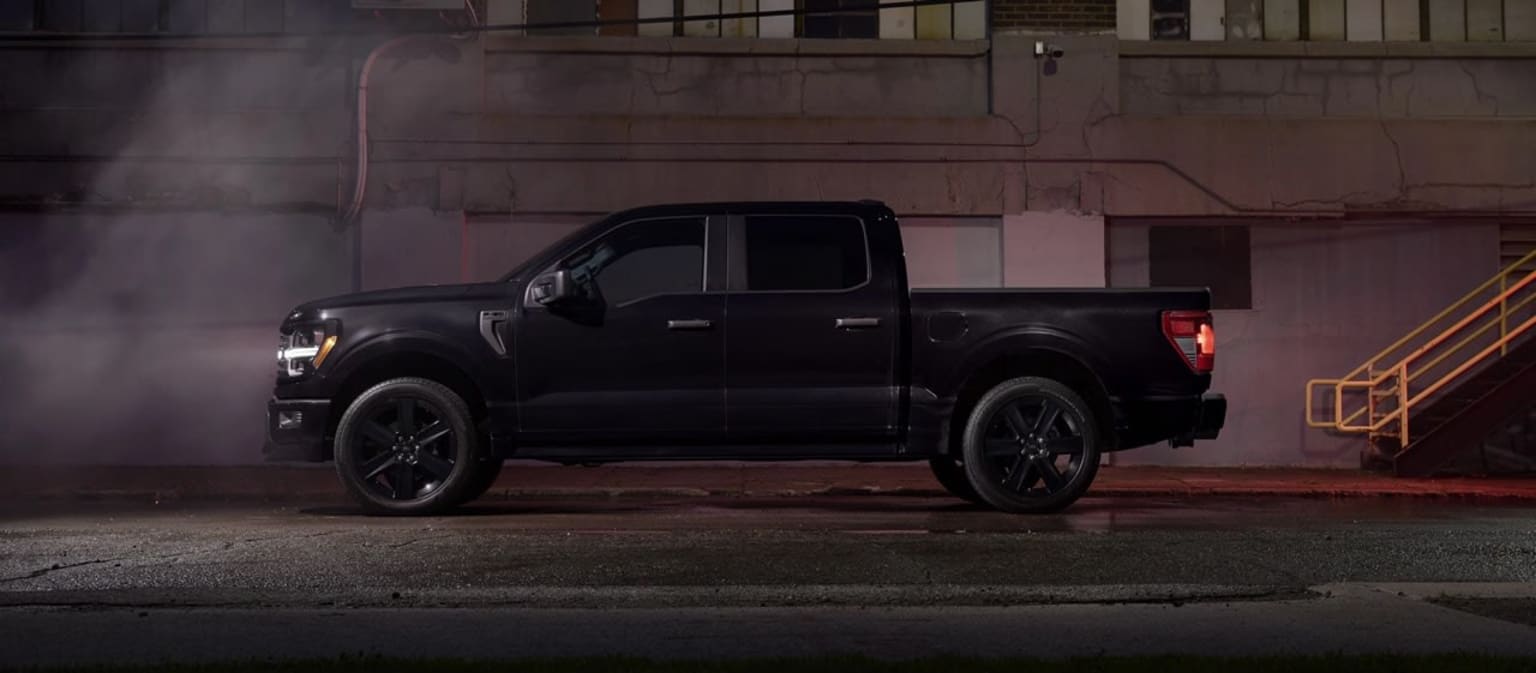 A large, black pickup truck in a dimly lit industrial setting with steam or smoke visible in the background.