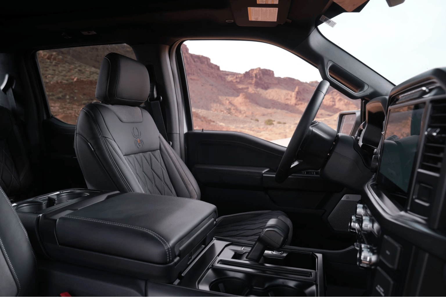 Interior of a vehicle with leather seats and a view of a rugged, mountainous landscape through the windshield.