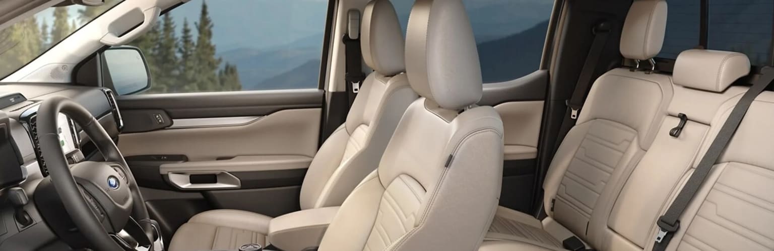 Interior of a vehicle with beige leather seats and a mountainous landscape visible through the windows.