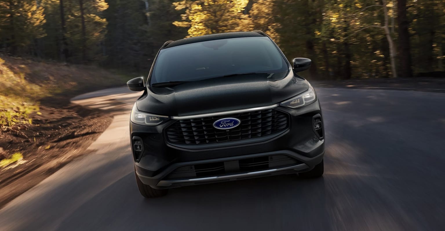 A black SUV driving on a winding forest road with vibrant autumn foliage.
