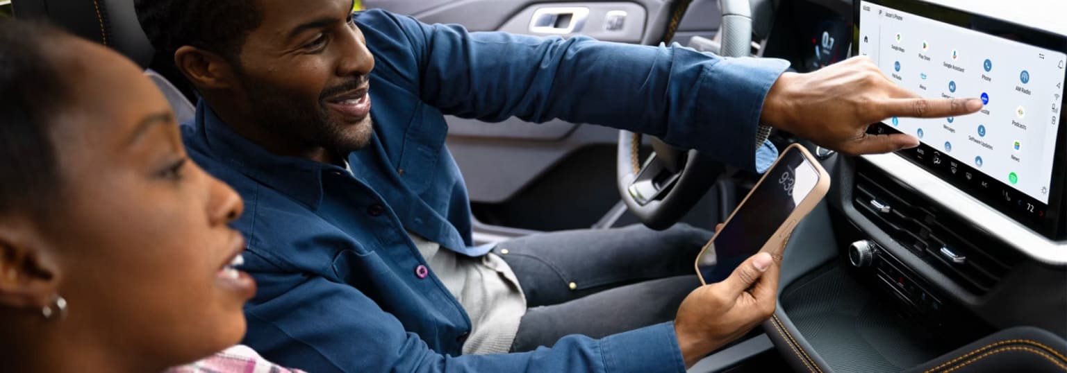 A person in a blue jacket is seated in the driver's seat of a car, looking attentively at the steering wheel and dashboard.