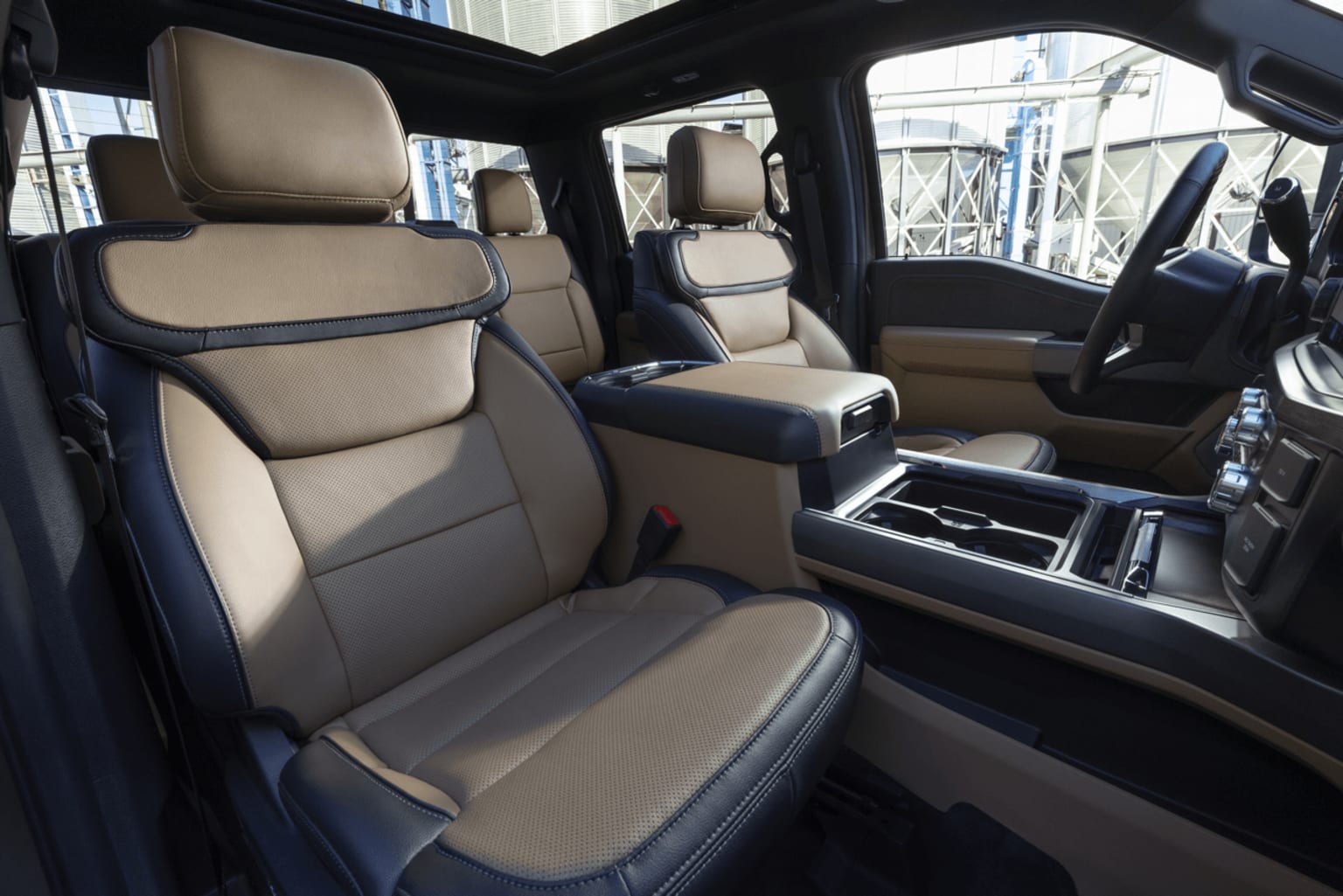 The image shows the interior of a vehicle, with beige leather seats and a center console in the foreground, and a cityscape visible through the windows in the background.