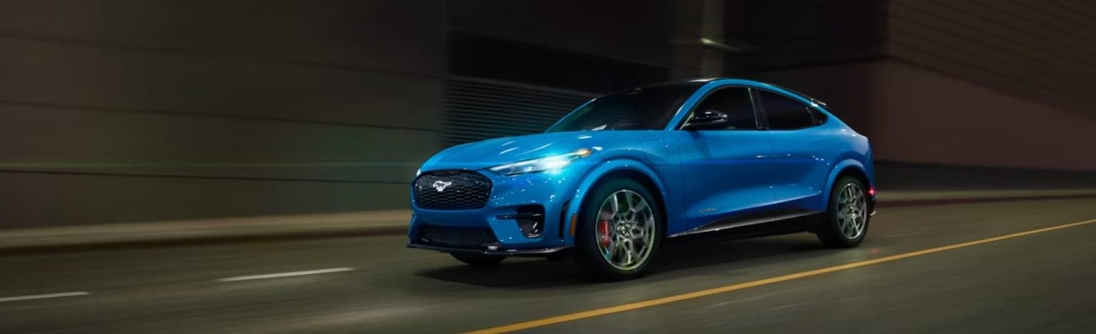 A blue electric SUV drives through a dark tunnel with illuminated headlights.