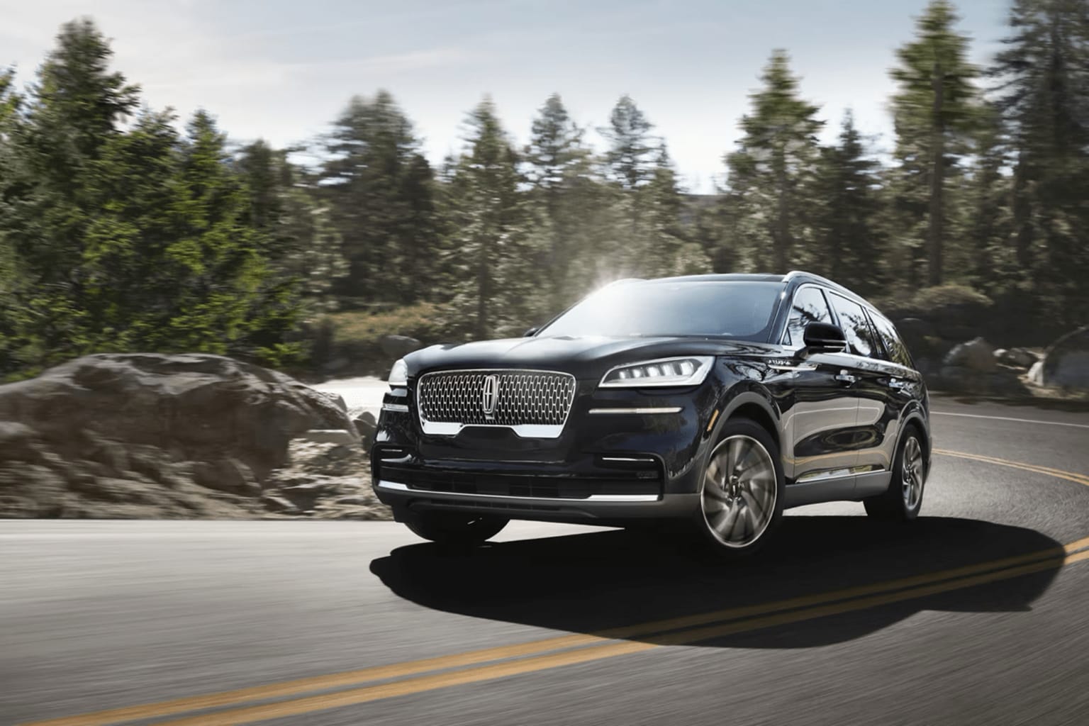 A sleek luxury SUV is driving down a winding road surrounded by a lush, forested landscape.
