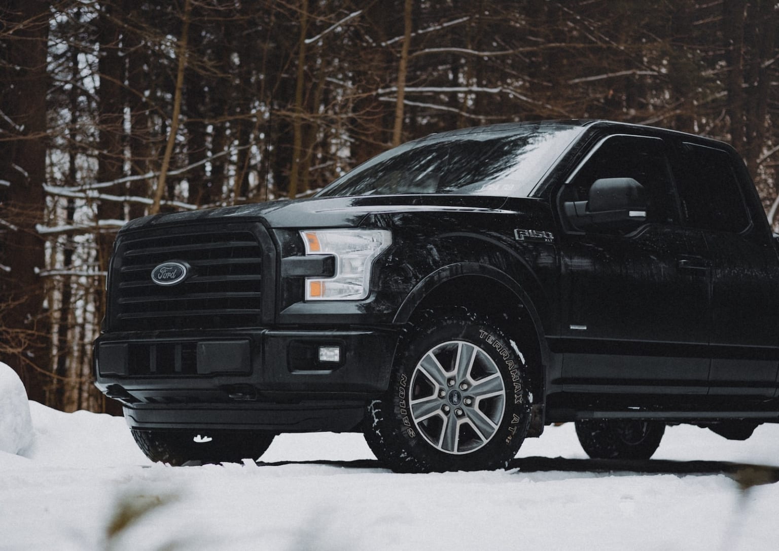 a black truck parked in the snow in front of a wooded area with snow on the ground and trees in the background