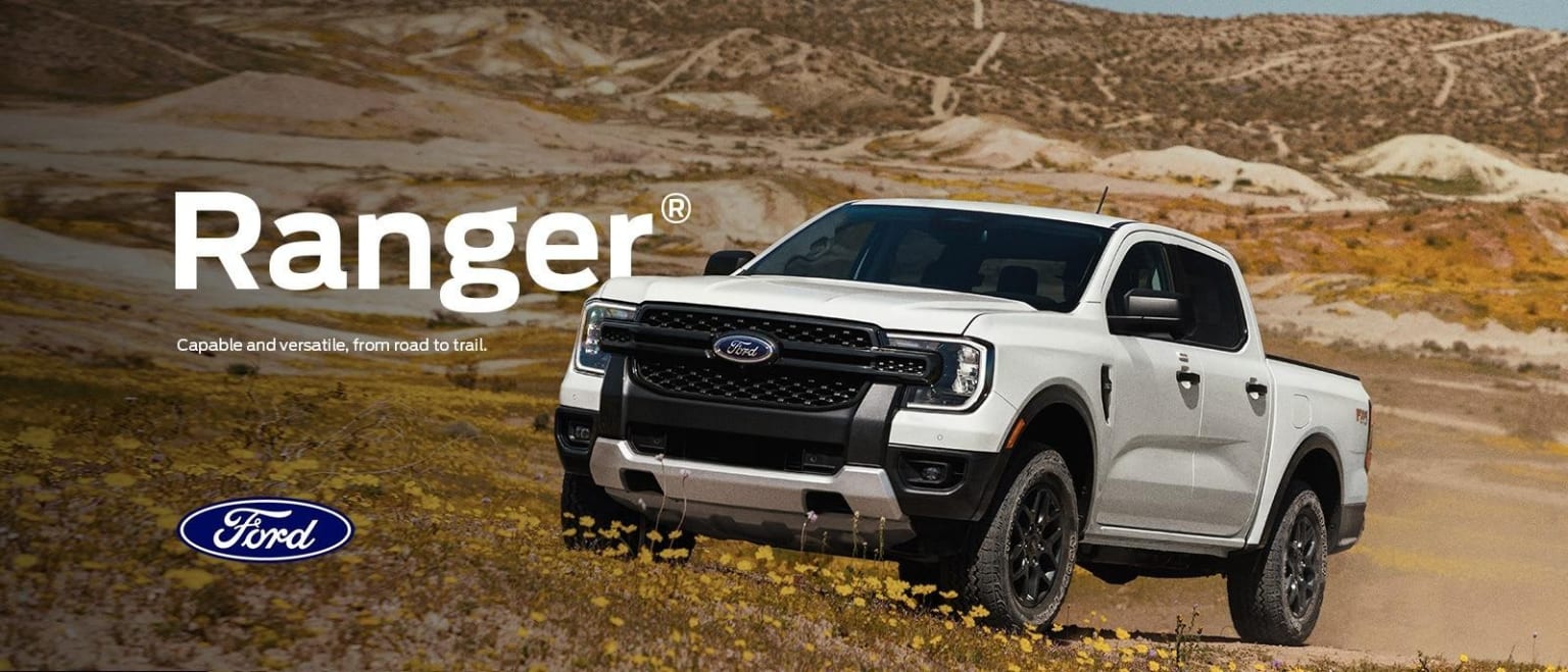 A white pickup truck is prominently featured in the foreground, set against a rugged, mountainous landscape in the background.