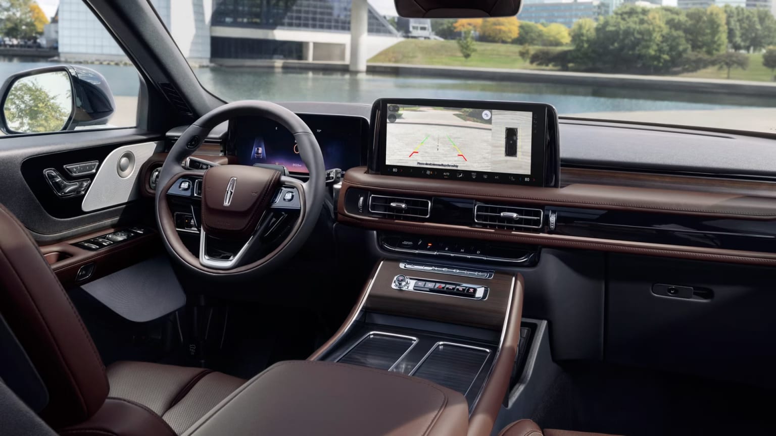 The image shows the interior of a modern, high-end vehicle with a large touchscreen display, a sleek dashboard, and a steering wheel. The background outside the vehicle appears to be a cityscape with buildings and greenery.