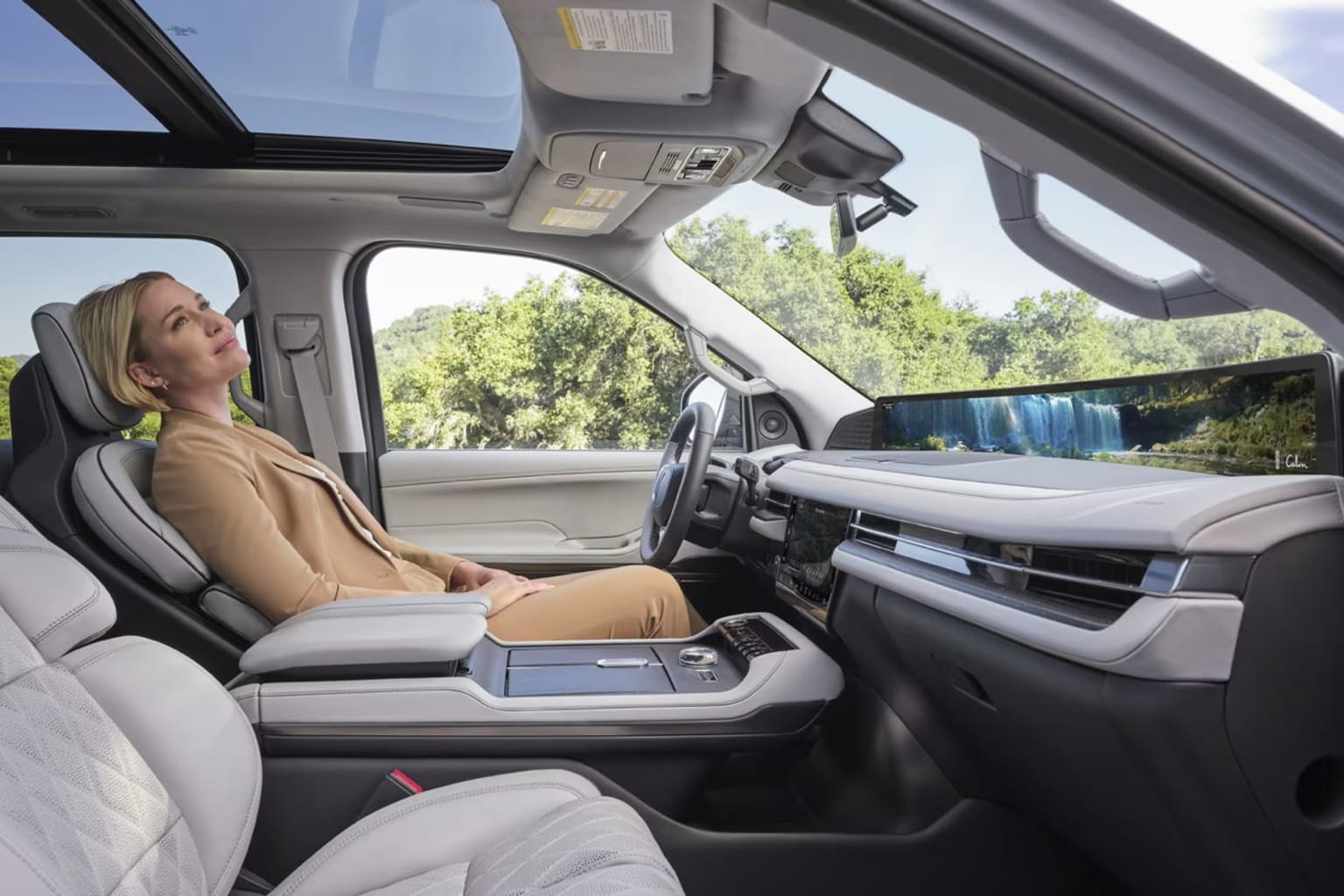 Interior of a vehicle with a person sitting in the driver's seat and a view of the surrounding landscape through the windshield.