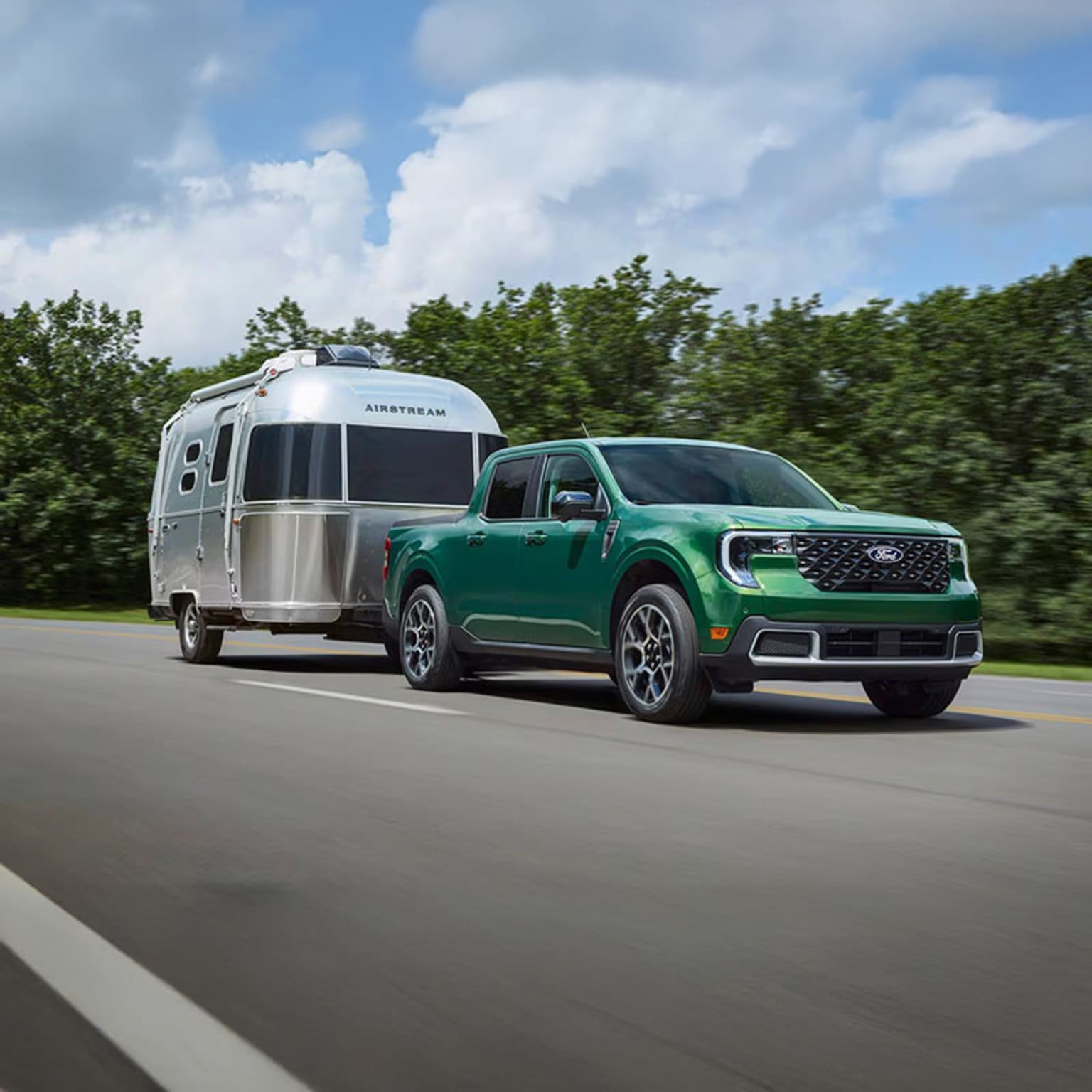 A green SUV is towing a silver trailer on a road surrounded by lush greenery and cloudy skies.