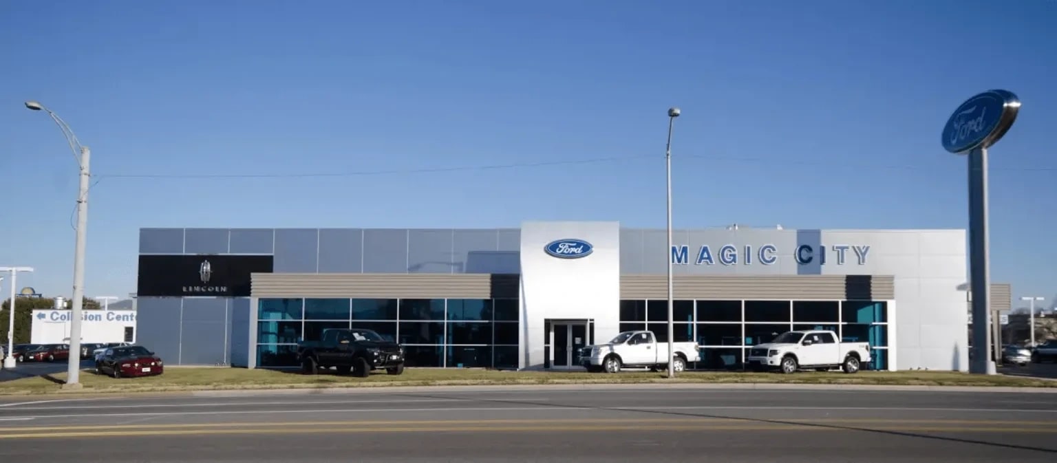 Several cars are parked in front of a modern dealership with a large logo sign in the background.