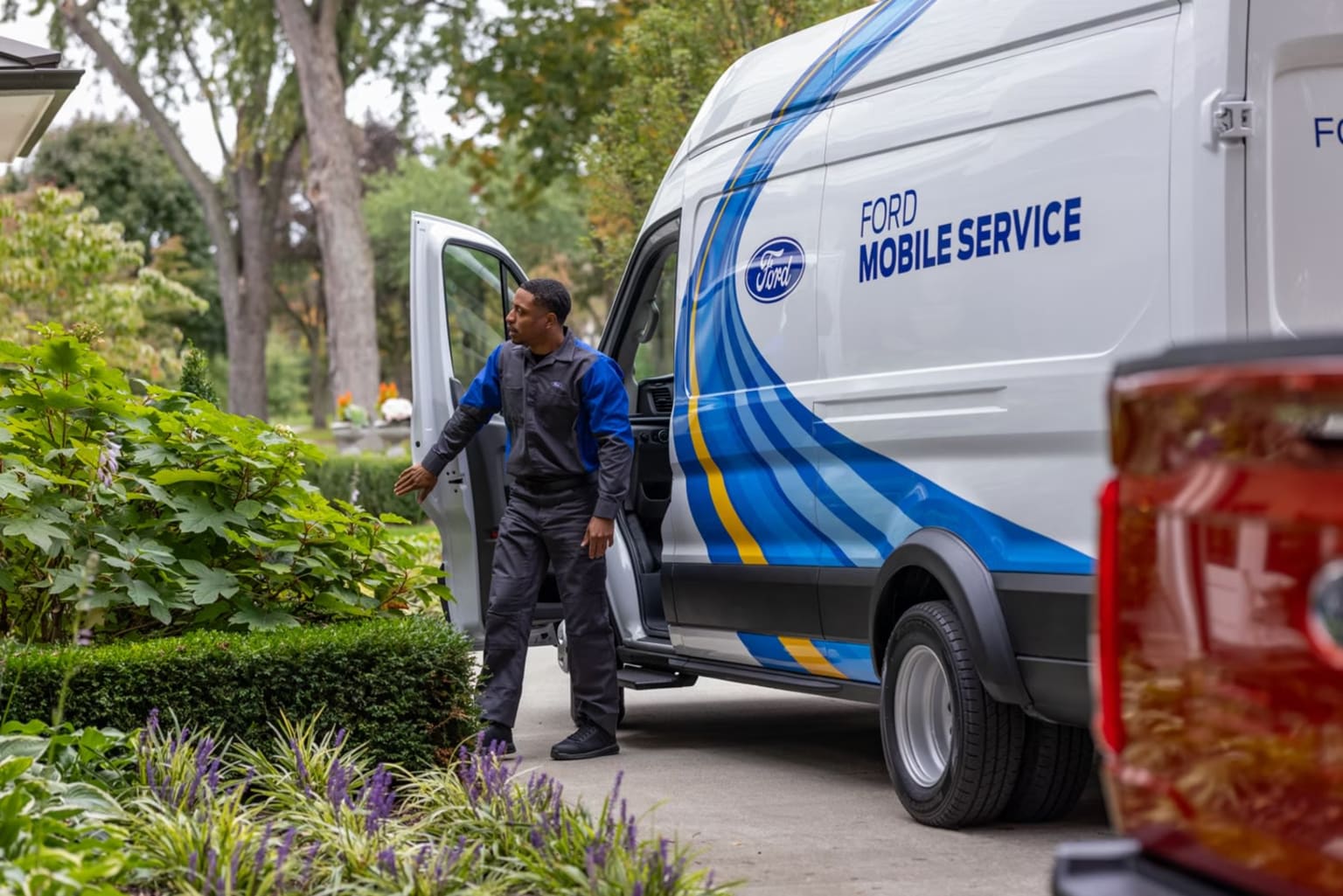 A person in a blue uniform is standing next to a white van with "MOBILE SERVICE" written on the side, surrounded by lush greenery and foliage.