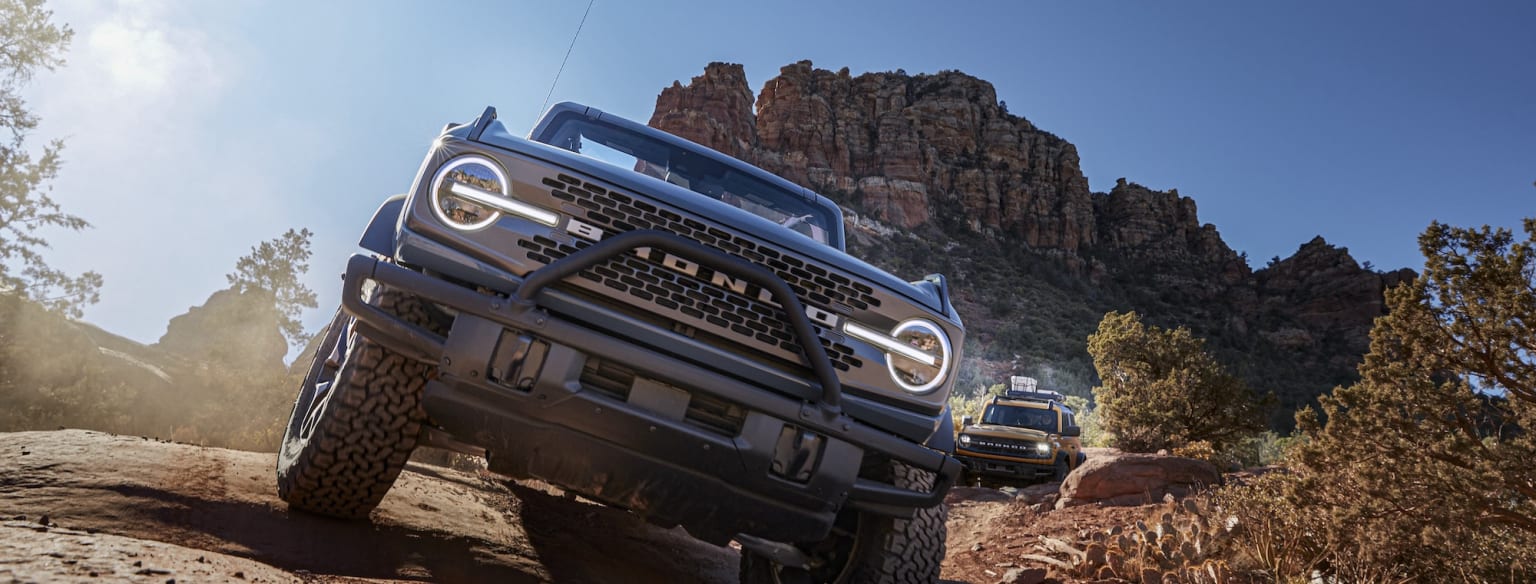 a couple of trucks driving down a dirt road next to some rocks and a mountain in the back ground