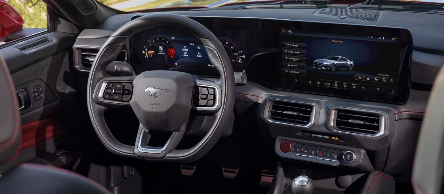 The image depicts the interior of a modern vehicle with a steering wheel, dashboard, and a large touchscreen display in the center console. The background indicates motion with a blurred outdoor scene.