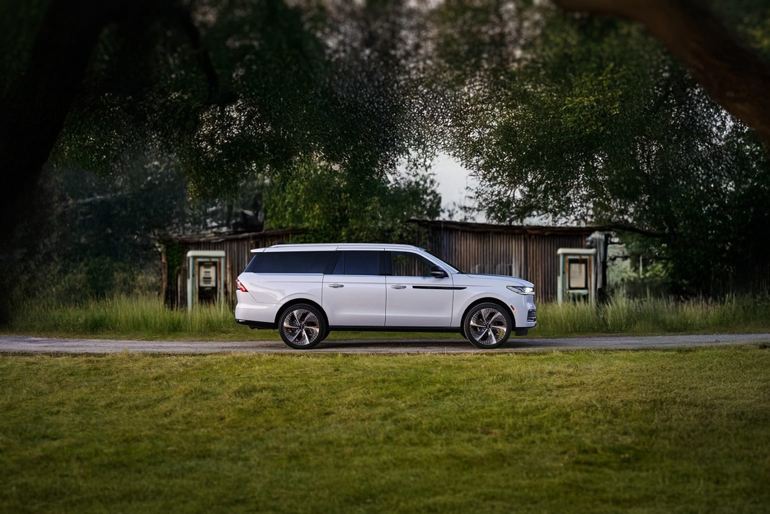 White SUV in a rural setting with trees and wooden structure
