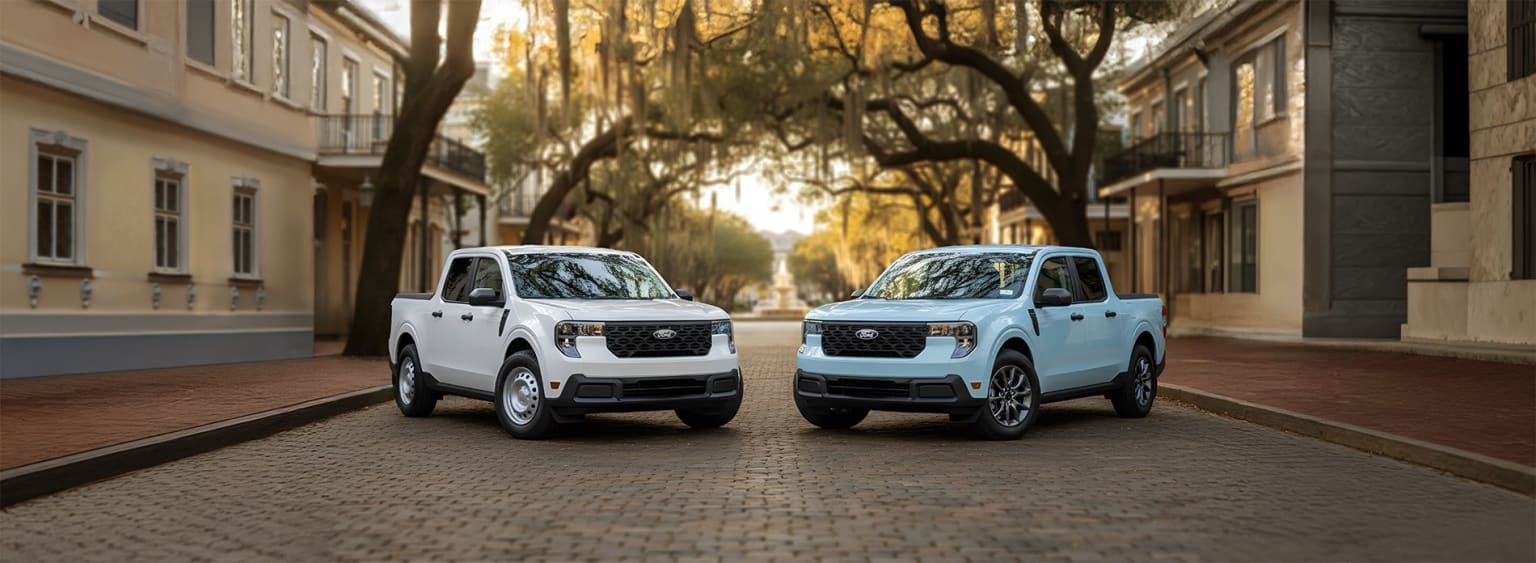 Two white compact utility vehicles parked on a brick-paved street, surrounded by lush, overhanging trees creating a warm, inviting atmosphere.