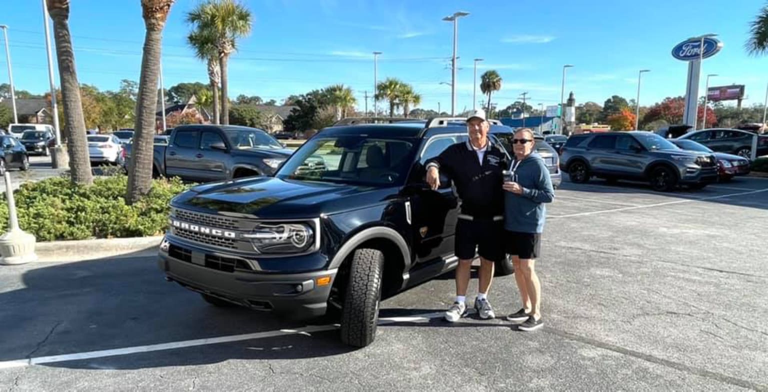 a man and woman standing in front of a truck in a parking lot with palm trees in the background