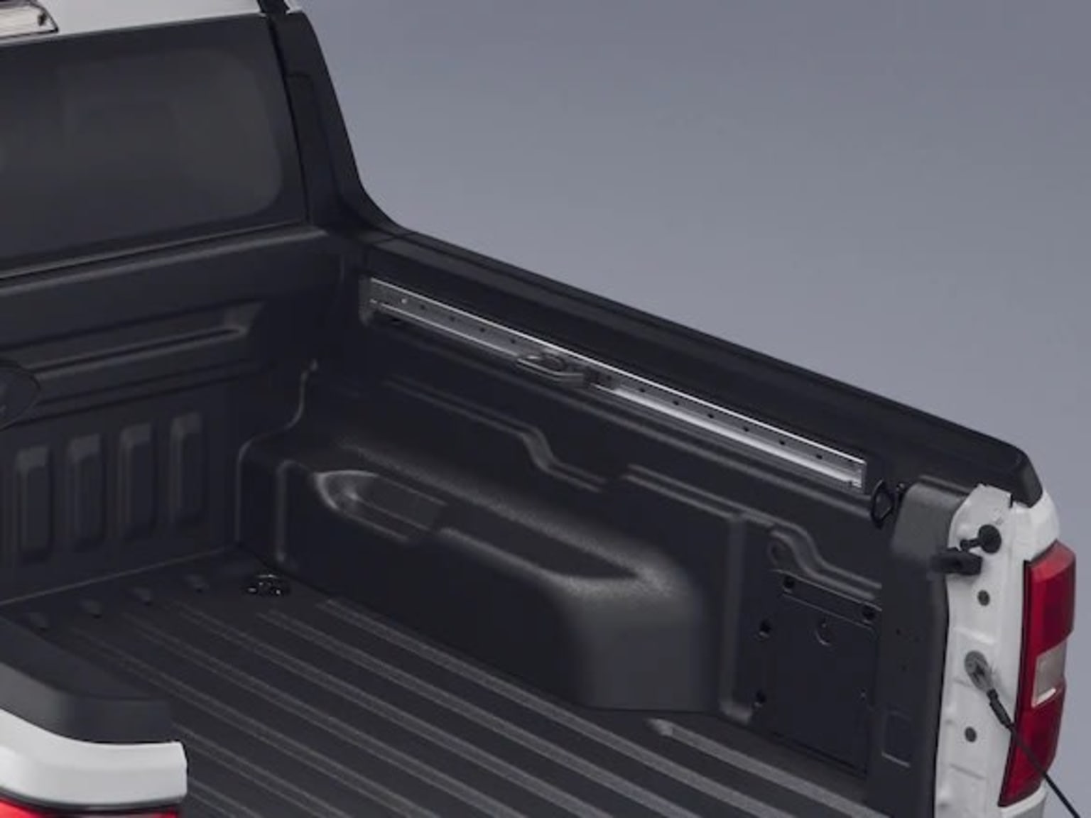 Truck bed with storage compartment and red taillight in the background.