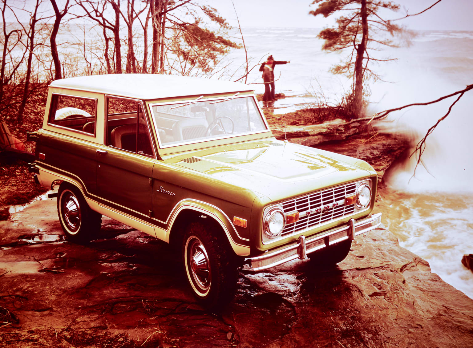 a green truck parked on top of a dirt hill next to a lake and a man standing on a cliff