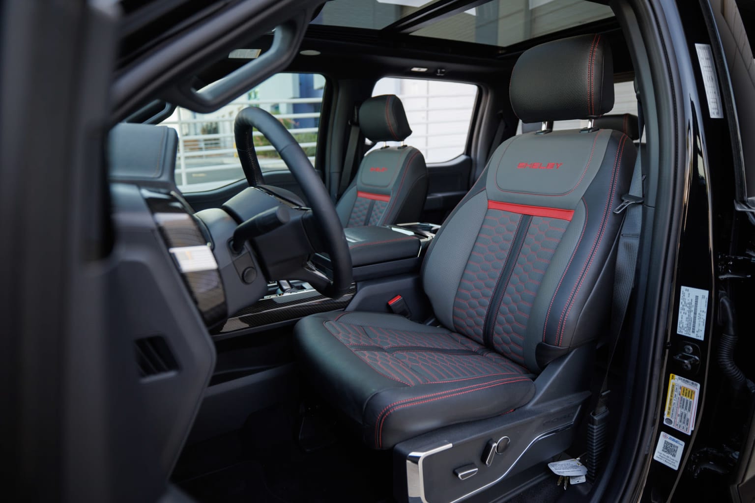 Interior of a vehicle featuring front seats with a black and red design, set in a modern, high-end setting.