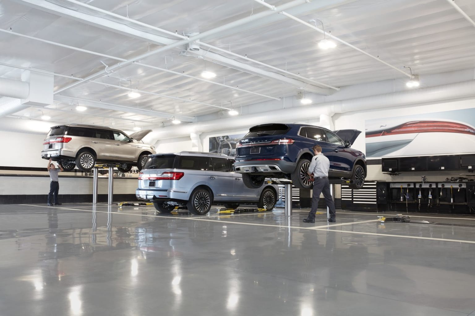 An image of a spacious and well-lit auto repair shop with several vehicles on lifts, including a large SUV and a smaller sedan, along with various tools and equipment visible in the background.