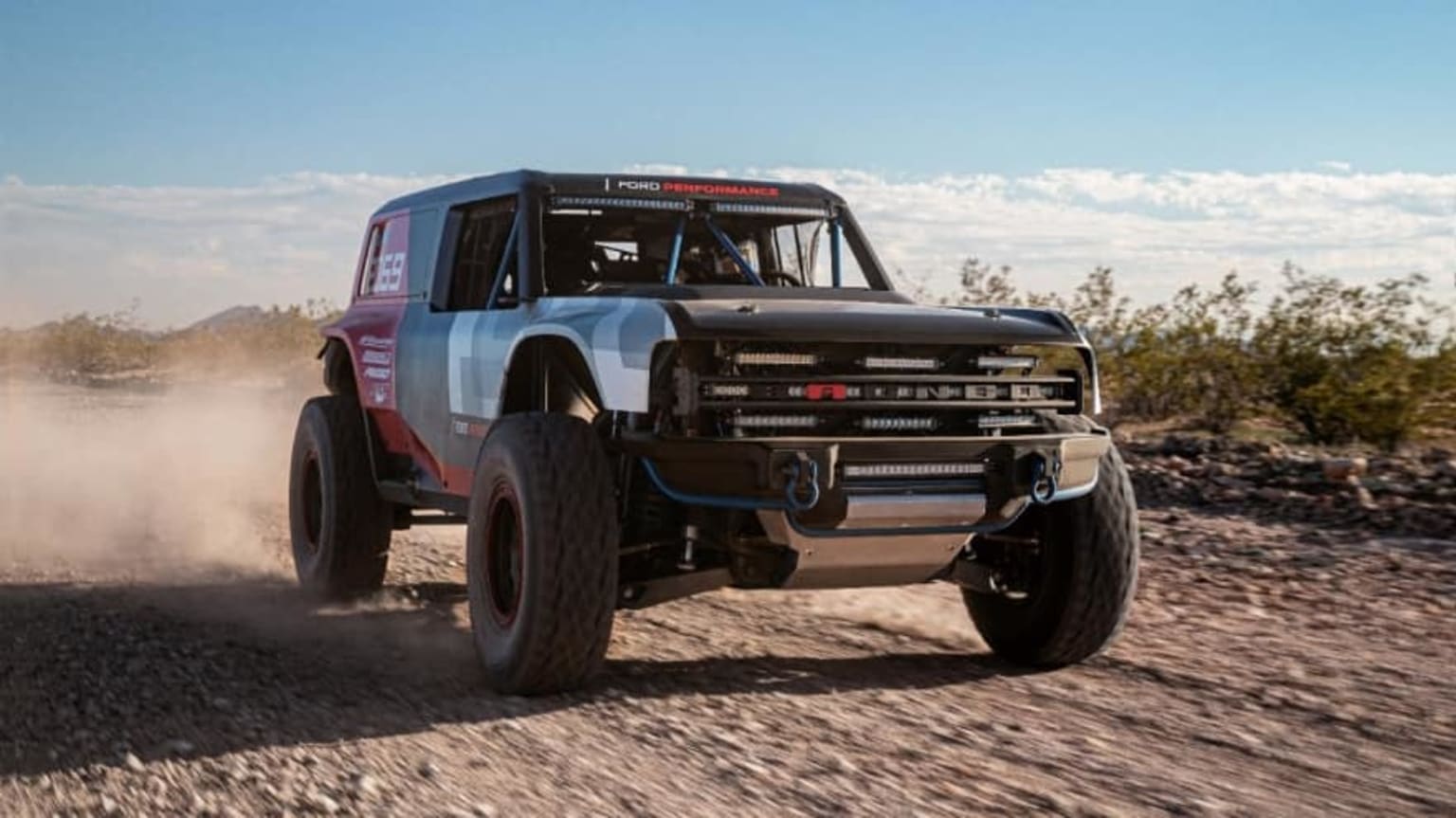 a truck driving down a dirt road with a sky in the backgrouund and a cloud of dust behind it