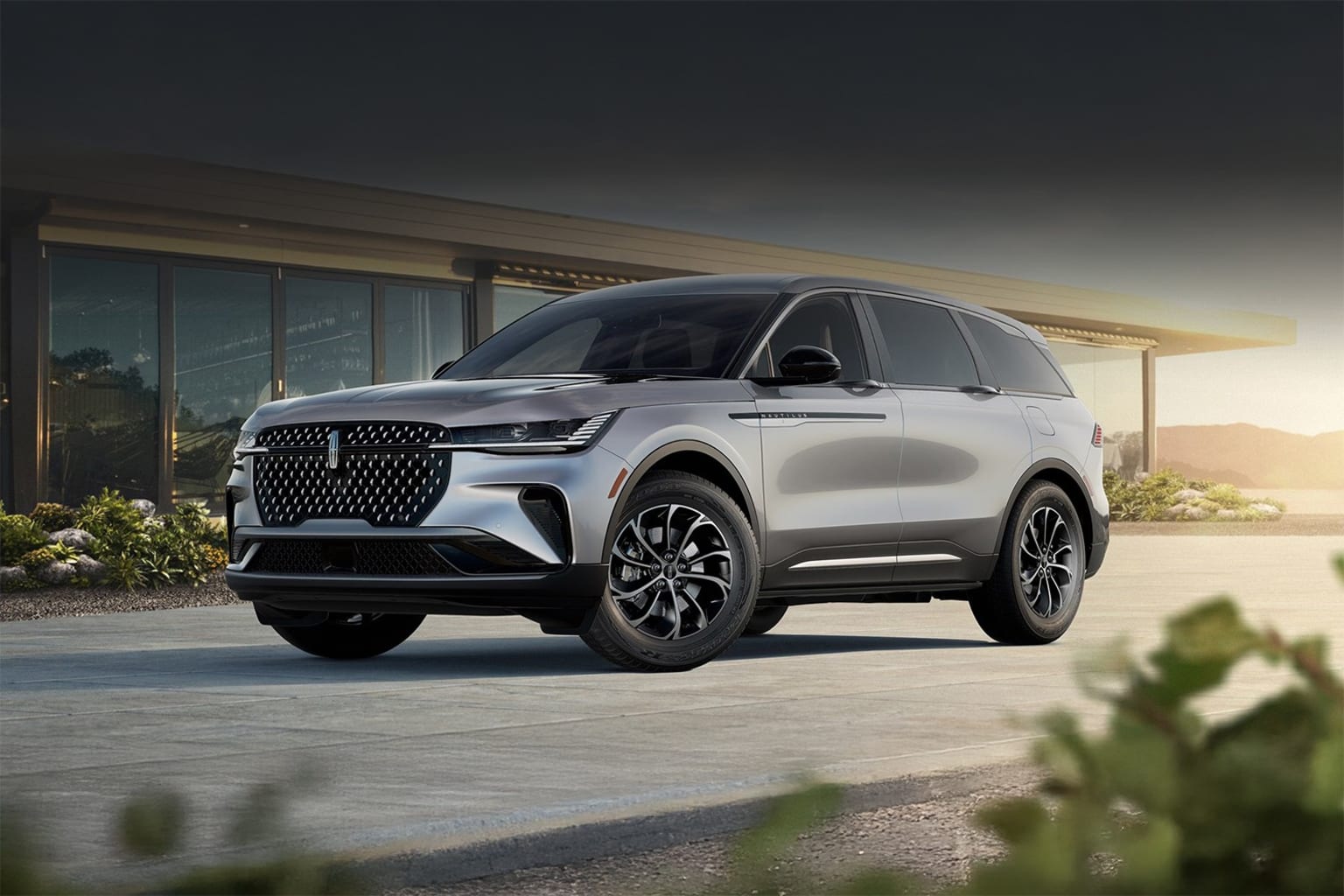 SUV in front of a contemporary building with lush greenery and a paved driveway.