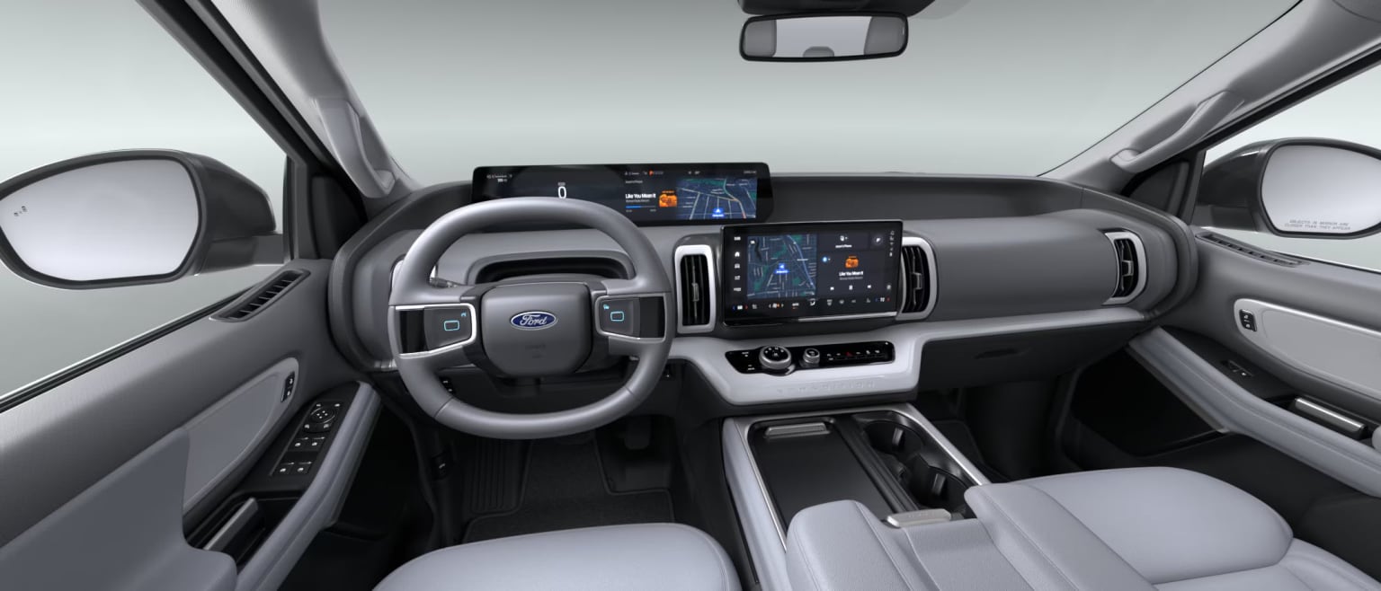 The image shows the interior of a modern vehicle, featuring a sleek and minimalist dashboard design with a large touchscreen display, various controls, and a steering wheel.