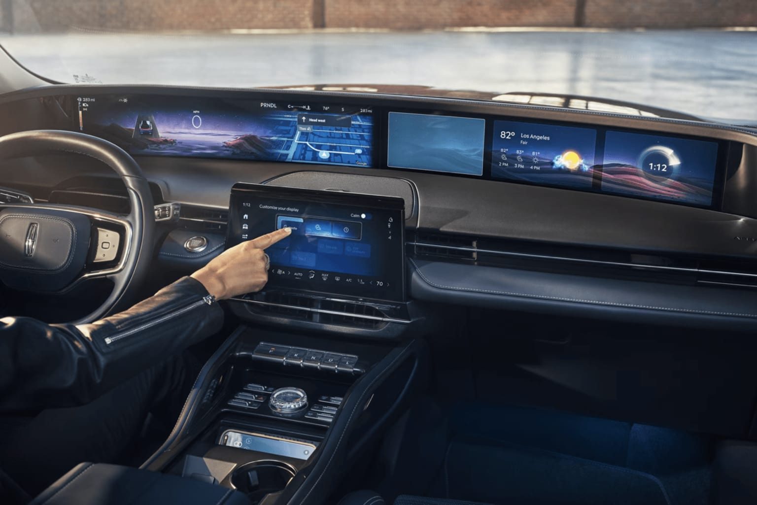 The image displays the interior of a modern vehicle, featuring a large digital display panel and various controls and buttons on the dashboard. A hand is visible, interacting with the touchscreen interface.